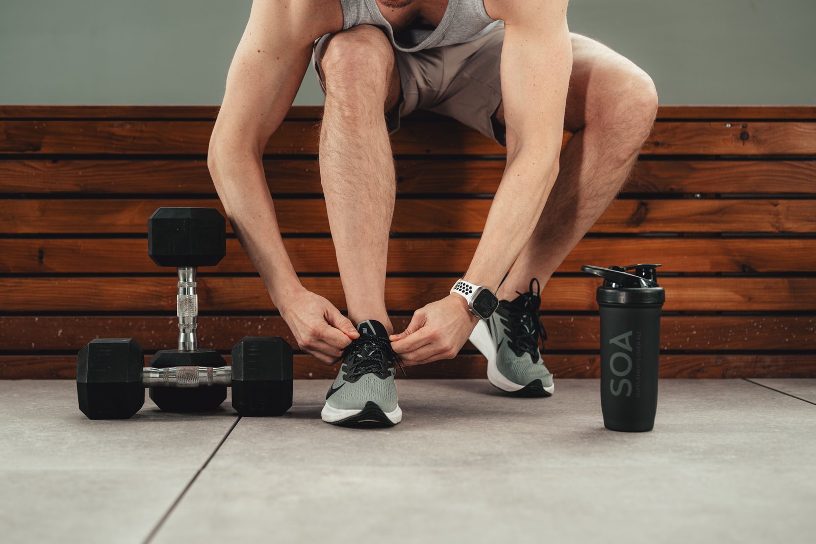 SOA Training – Athlet bindet Schuhe vor dem Workout mit Kurzhanteln und Shaker